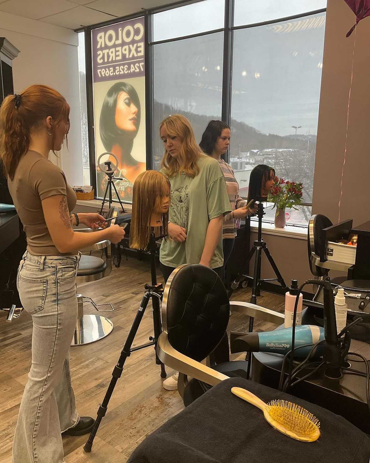 Students practicing hairdressing on mannequins in a beauty school classroom.